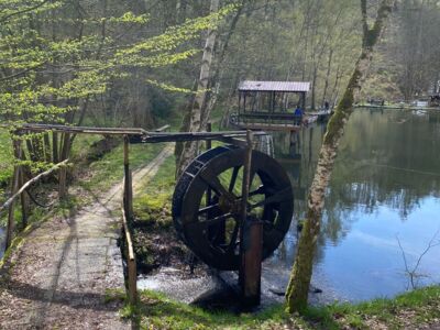 Das Foto zeigt ein altes Wasserrad und einen Steg über einen Bach.