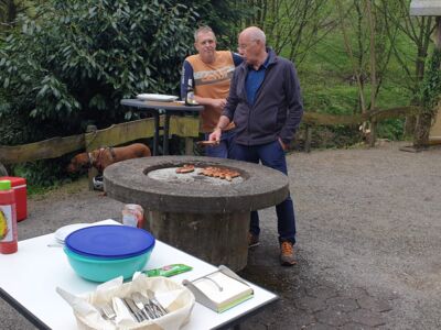 Auf dem Foto sind zwei Männer am Grill zusehen, auf dem Würstchen gegrillt werden