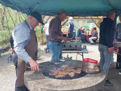 Auf dem Foto ist der Grill mit Grillfleisch und Helfern zu sehen.