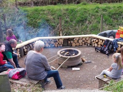 Kinder und Erwachsene am offenen Grillfeuer beim Stockbrotbacken