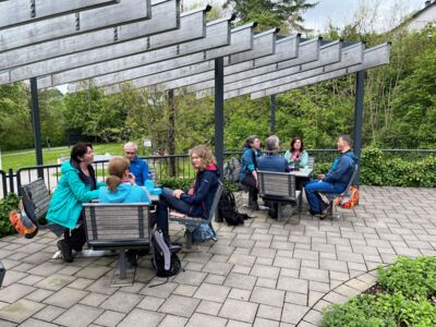 Ein Teil der Wandergruppe bei der Rast an Tischen und Bänken im Kurpark Eckenhagen.