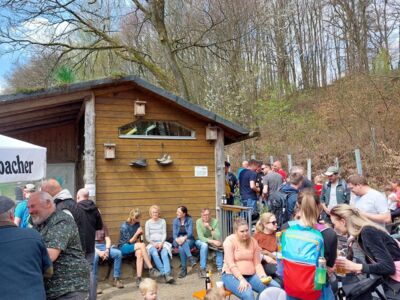 Das Foto zeigt viele Besucher an Stehtischen und Sitzbänken. Im Hintergrund ist das Toilettengebäude mit einem Freisitzbereich zu sehen.