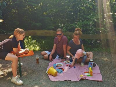 Auf dem Foto ist eine Familie zu sehen. Ein Kleinkind spielt auf einer Decke.