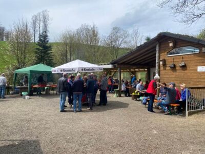 Auf dem Foto ist das Areal der SGV-Hütte mit Sitzbereich, Grillstation und Stehtisch zu sehen. Einige Personen halten sich dort bereits auf.